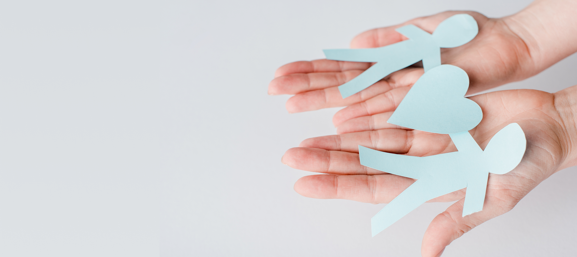 Zwei Hände halten hellblaue, aus Papier ausgeschnittene Figuren von Menschen und einem Herzen